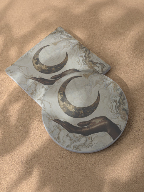 A ceramic coaster featuring a bronze-colored hand reaching toward an antiqued gold crescent moon against a swirling ivory and gold marble background, available in round and square shapes with cork backing.